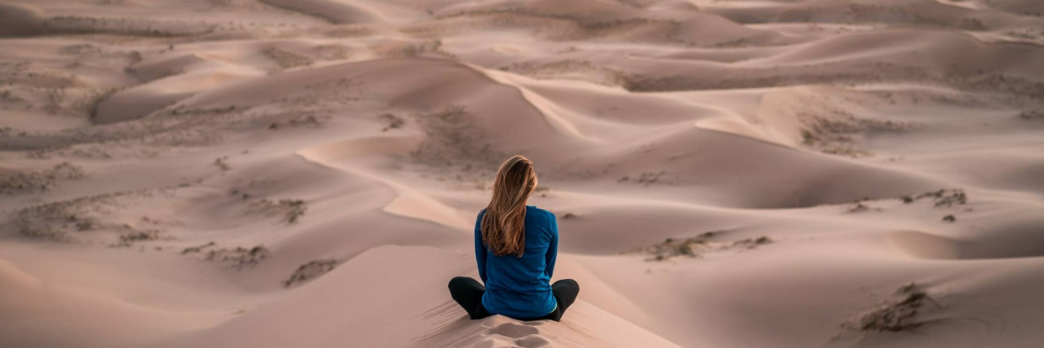 Eine Frau sitzt auf einer Sanddüne und schaut in die sich vor ihr erstreckende Wüste.